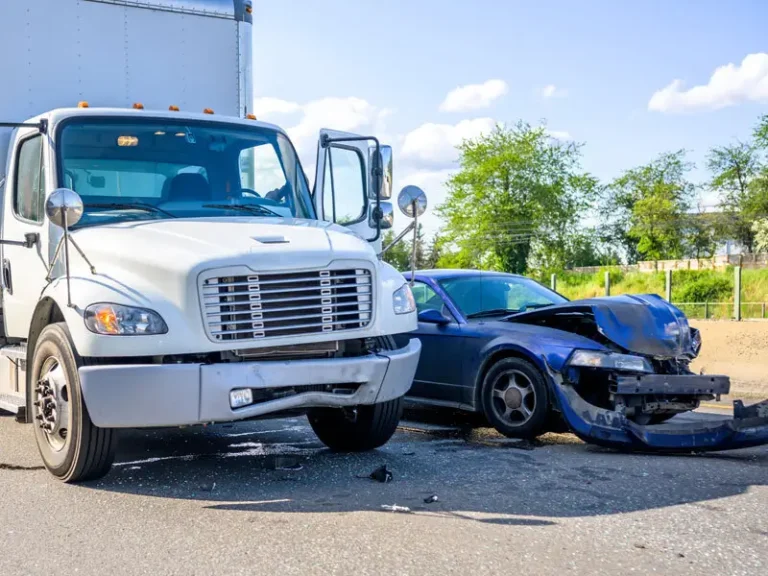A white truck and a blue car involved in a collision on a road, with visible damage to the car's front.