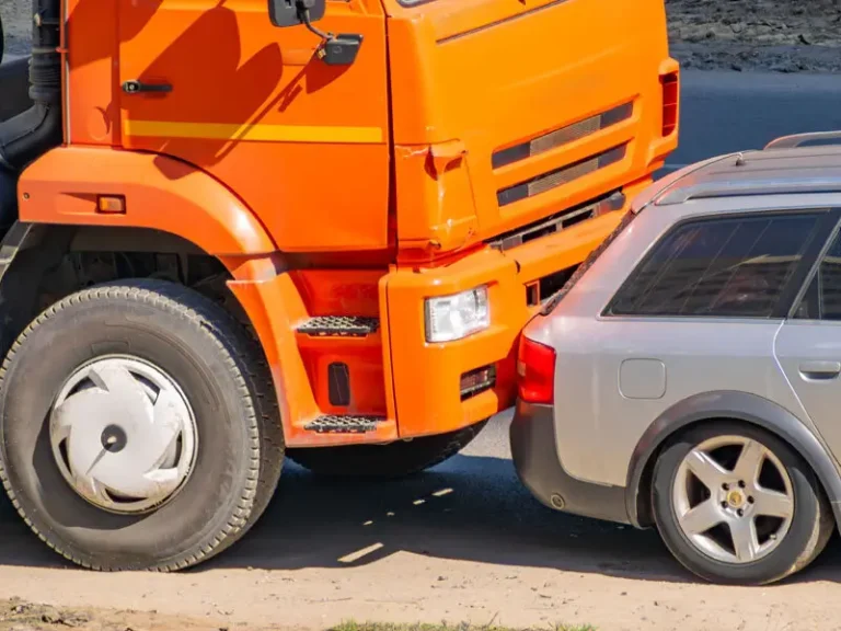 An orange truck has rear-ended a silver car on a road.