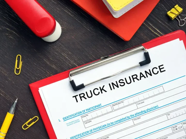 Clipboard with "TRUCK INSURANCE" form, pen, and office supplies on a wooden desk.