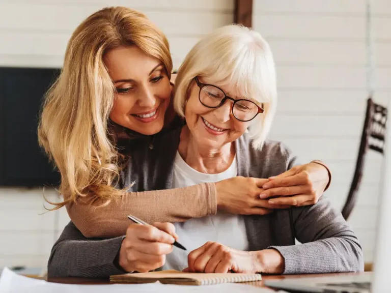 Two women, one younger, writing on paper, with an elderly woman watching.