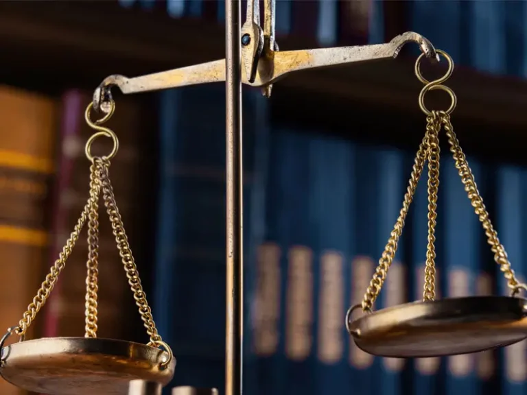 Close-up of a golden balance scale with a blurred bookshelf background.