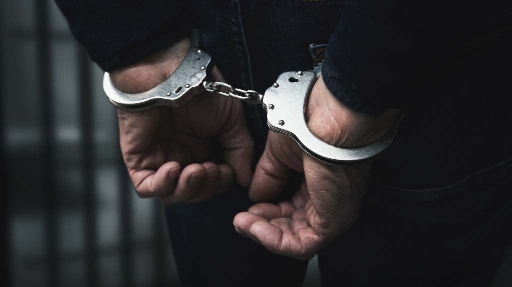 arrested man with cuffed hands behind prison bars