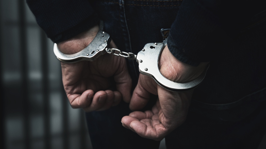 arrested man with cuffed hands behind prison bars