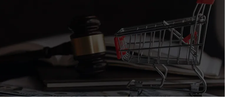 Small empty shopping cart beside a wooden judge's gavel on dark surface.
