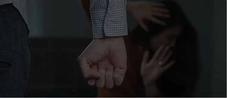 Close-up of a clenched fist in foreground with a distressed woman shielding her face in background.