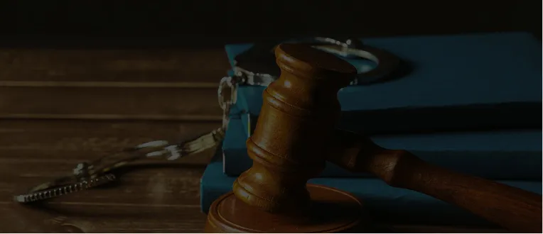 Wooden judge's gavel resting on a desk with blue law books and metal handcuffs.
