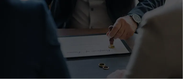 Two people at a table with a man stamping a document, two rings beside it.