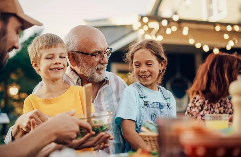 Multigenerational family enjoying an outdoor meal together at sunset with warm string lights.