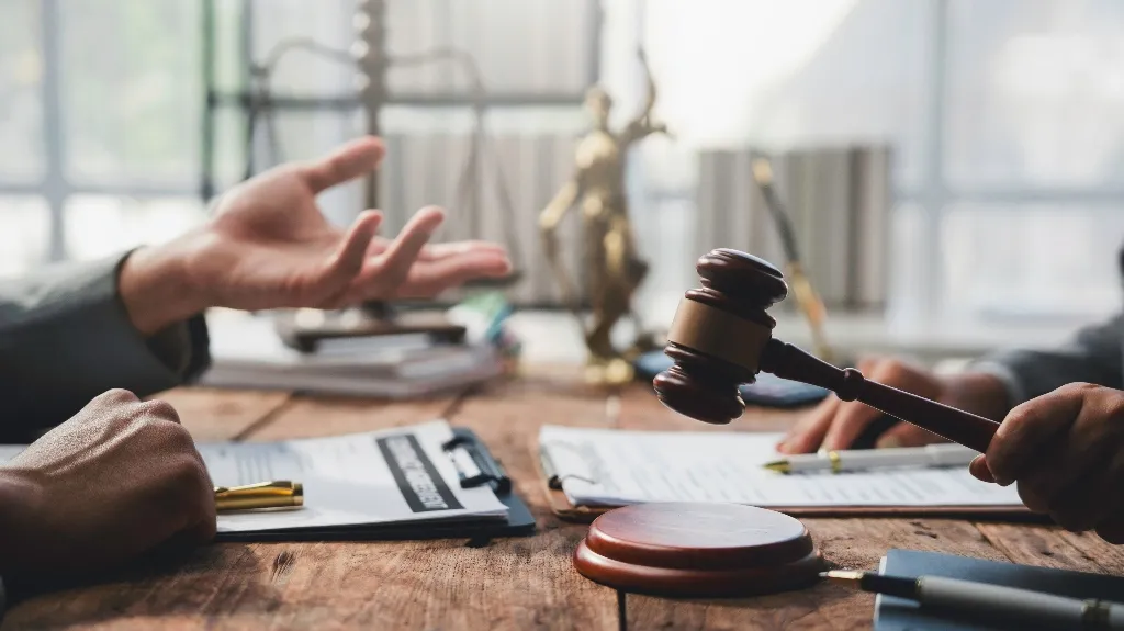 Two individuals engaged in a legal discussion with a wooden gavel and legal documents on a wooden table.