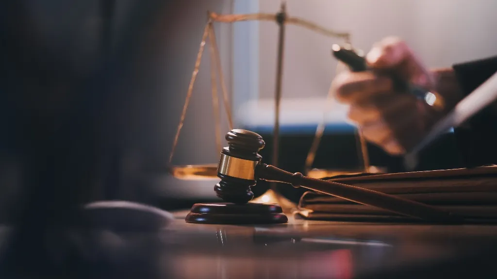 Close-up of a wooden judge's gavel and brass scales of justice on a desk.