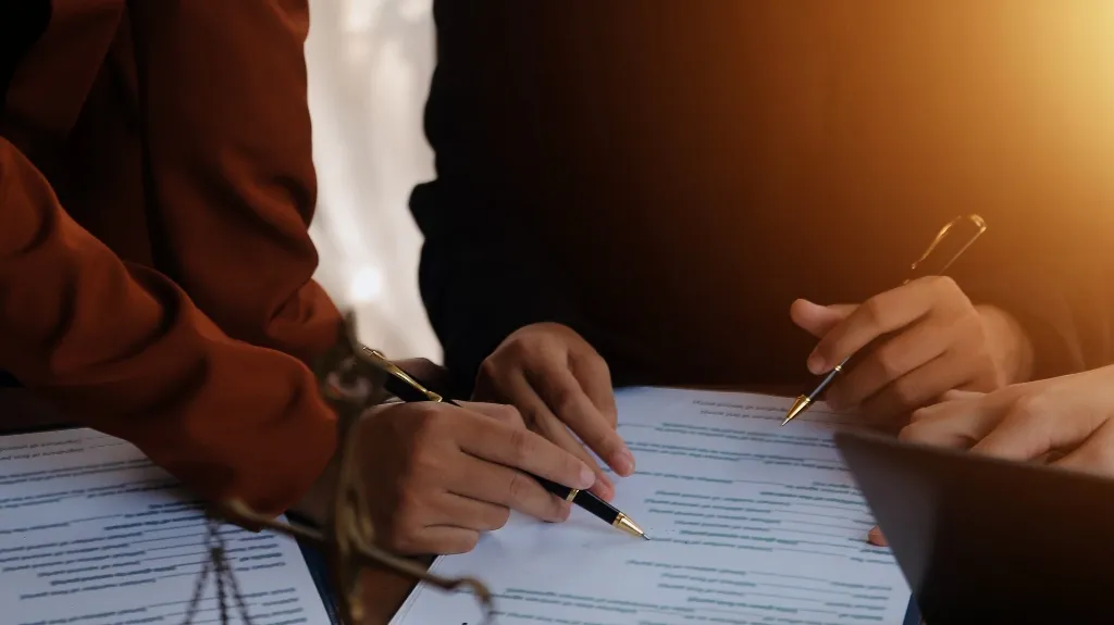 Two individuals reviewing and annotating documents with pens under warm lighting.