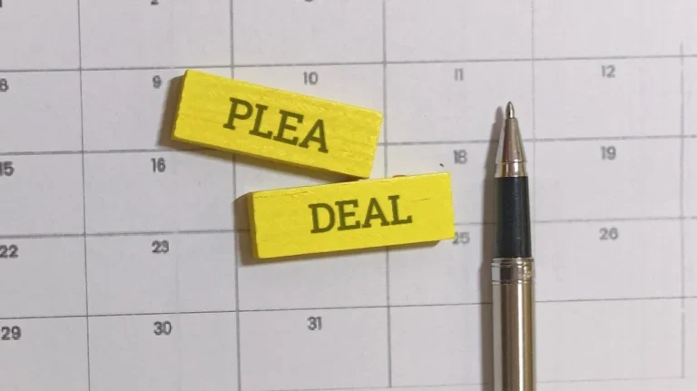 Close-up of a calendar with yellow wooden blocks labeled "PLEA" and "DEAL" and a black and silver pen.