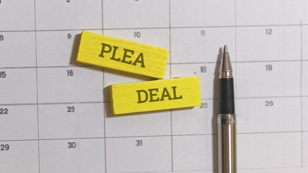 Close-up of a calendar with yellow wooden blocks labeled "PLEA" and "DEAL" and a black and silver pen.