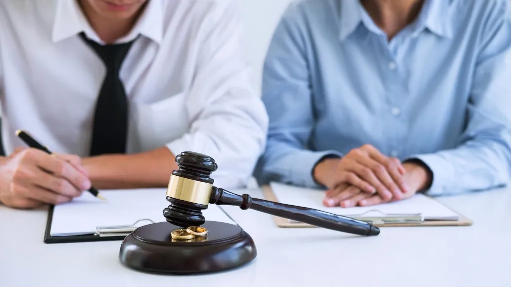 Two individuals seated at a table with legal documents, a judge's gavel, and wedding rings.