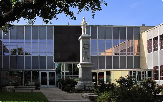 White stone soldier statue monument in front of reflective glass building under clear blue sky.