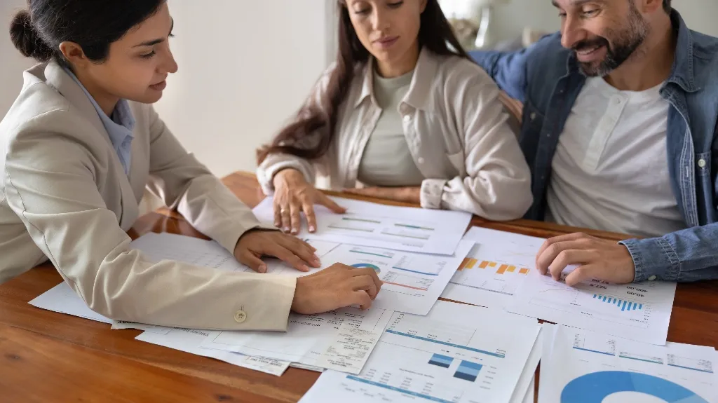 Three professionals reviewing financial charts and documents on a wooden table.