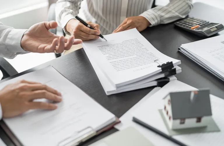 Two professionals reviewing and signing documents on a dark office desk.