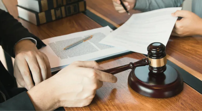 Hands holding a wooden gavel and reviewing legal documents on a wooden table.