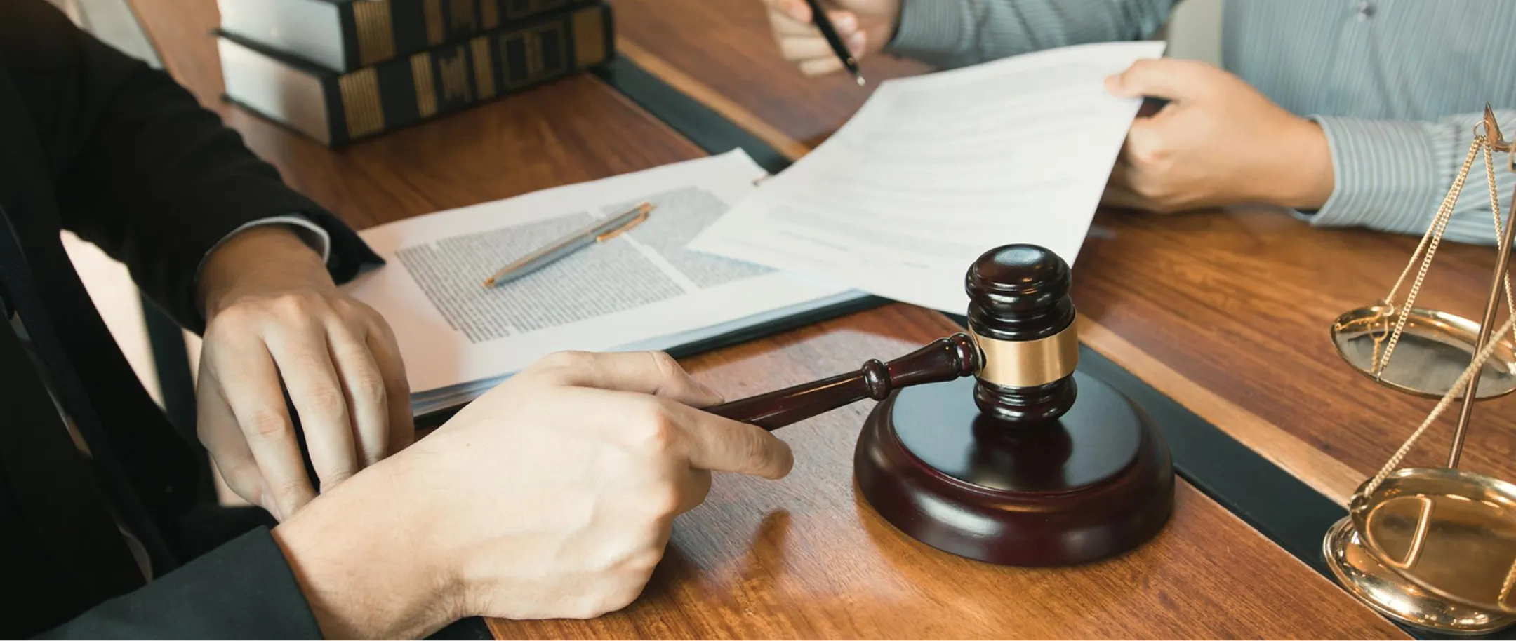 Two people reviewing legal documents with a judge's gavel and scales of justice on wooden table.