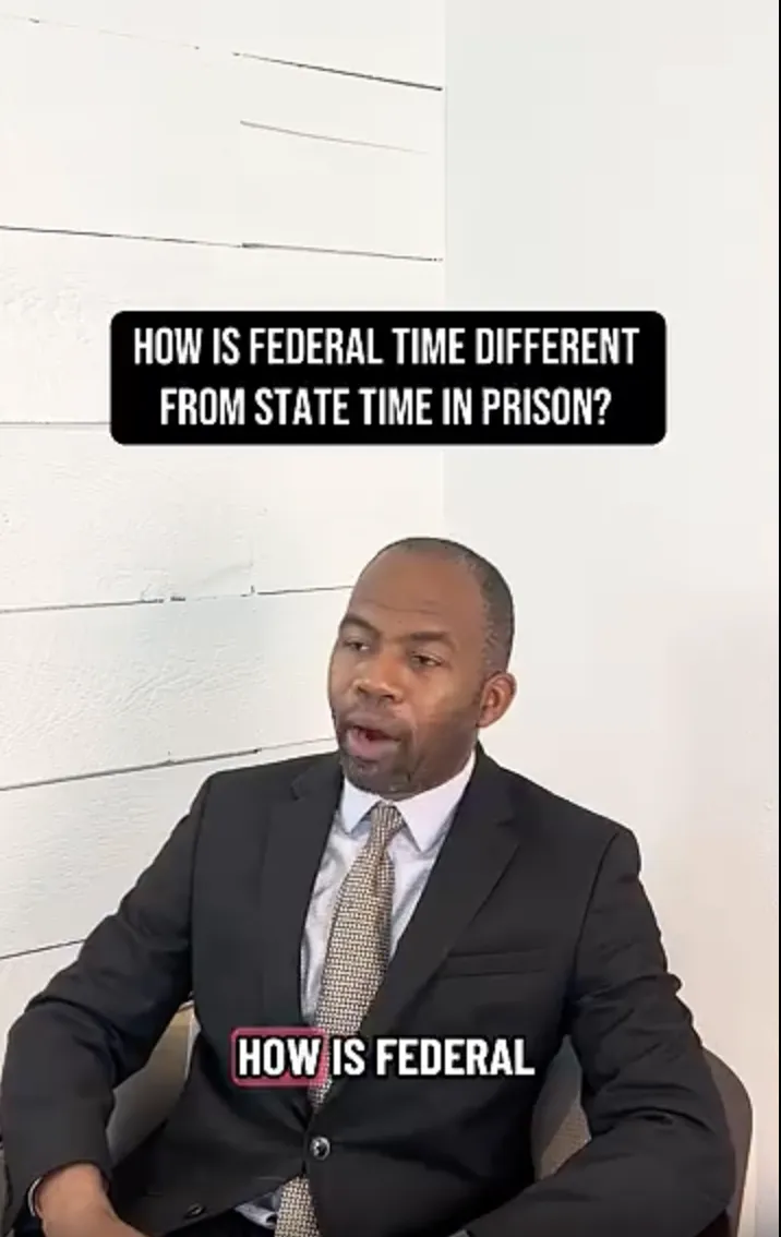 Man in a dark suit and patterned tie seated against a white paneled wall with text about federal versus state prison time.