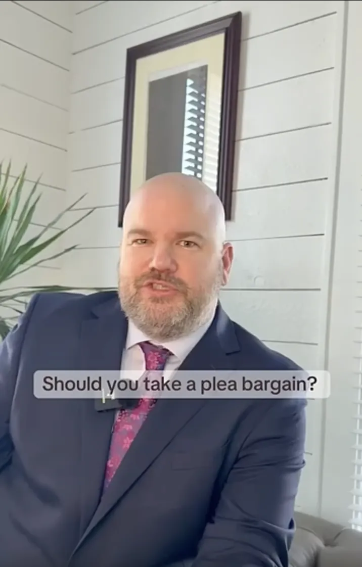 Professional man in suit and tie seated indoors with text overlay "Should you take a plea bargain?