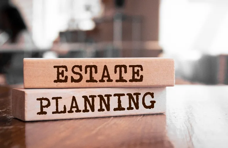 Two wooden blocks stacked on a wooden surface with the words "ESTATE PLANNING" printed in brown.