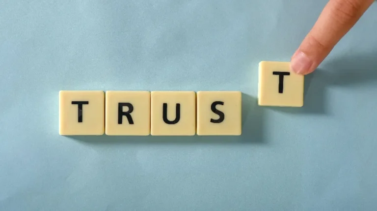 Hand placing a letter tile "T" to complete the word "TRUST" on a blue background.