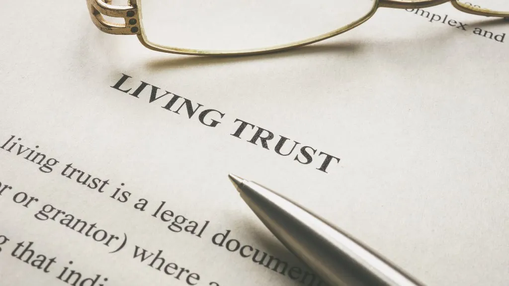 Close-up of a living trust legal document with a silver pen and reading glasses.