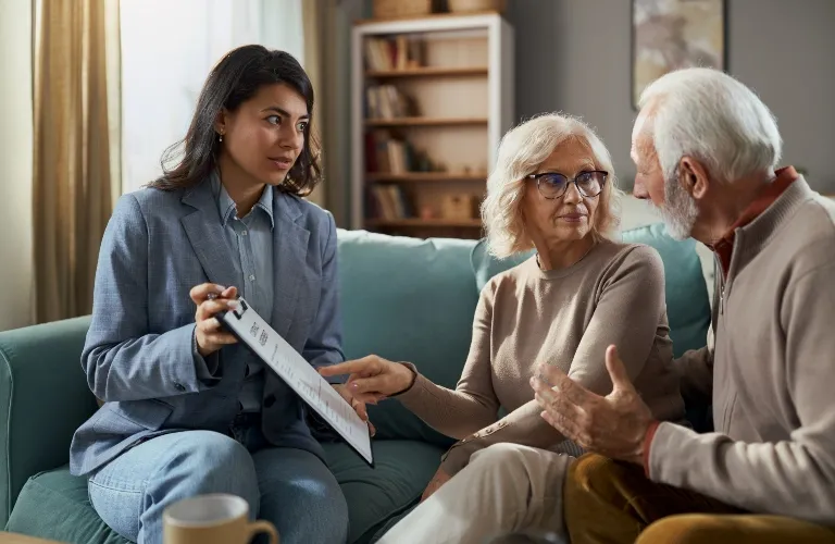 Professional woman discussing documents with elderly couple in a living room setting.