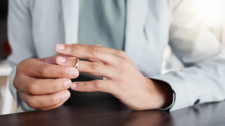Close-up of a person removing a gold ring from their finger, wearing a light gray shirt.
