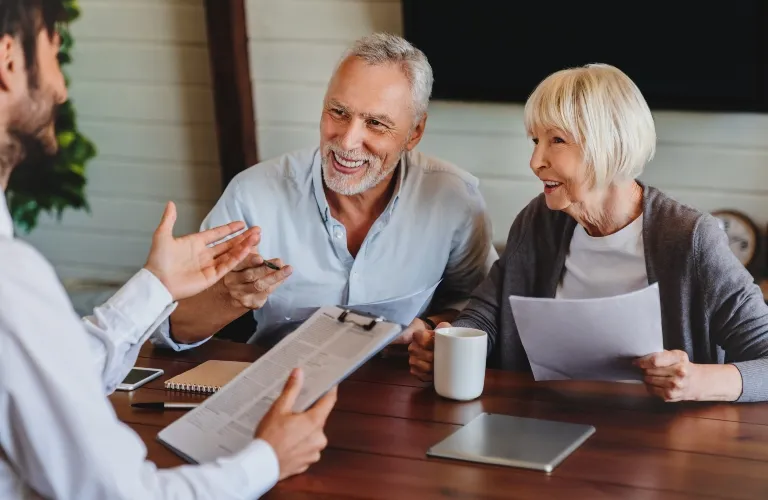 Two elderly individuals engaged in a discussion with a professional holding a clipboard at a wooden table.