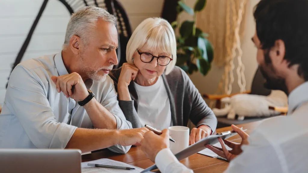 Three adults engaged in a discussion, reviewing documents at a wooden table indoors.