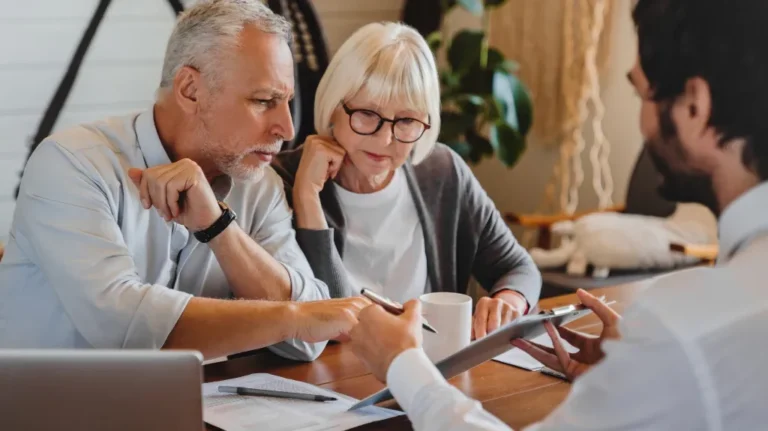 Two elderly individuals attentively reviewing documents with a professional in a modern office setting.