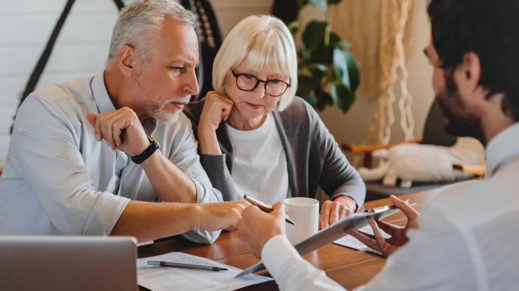 Two elderly individuals attentively reviewing documents with a professional in a modern office setting.