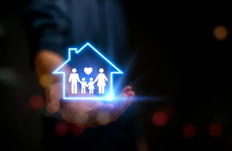 Hand holding glowing blue house icon with family figures and heart inside on dark background.