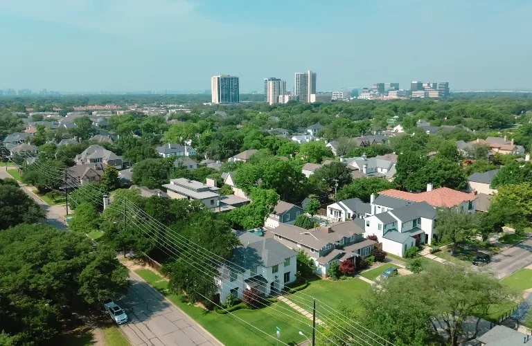 Aerial view of a suburban neighborhood with green trees and multi-story buildings in the background.