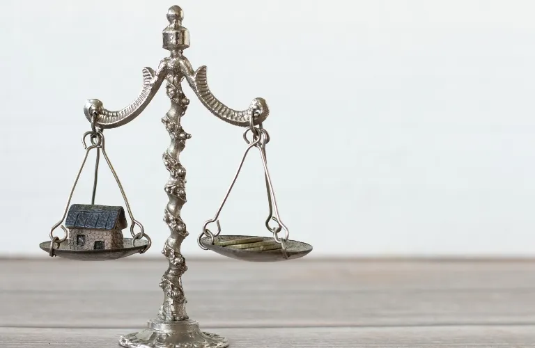 Antique silver balance scale with a small house model on one side and coins on the other.