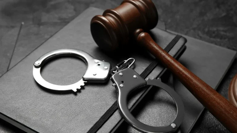 Wooden judge gavel and metal handcuffs resting on black notebooks.