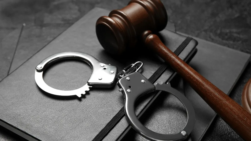 Wooden judge gavel and metal handcuffs resting on black notebooks.