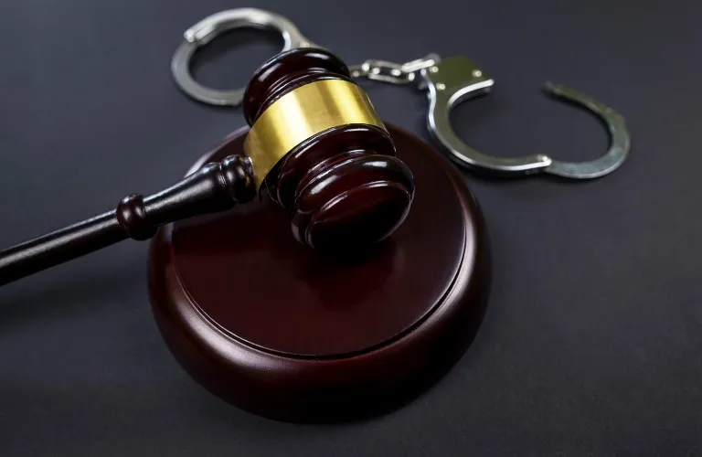 Wooden judge's gavel with brass band resting on sound block next to metal handcuffs.
